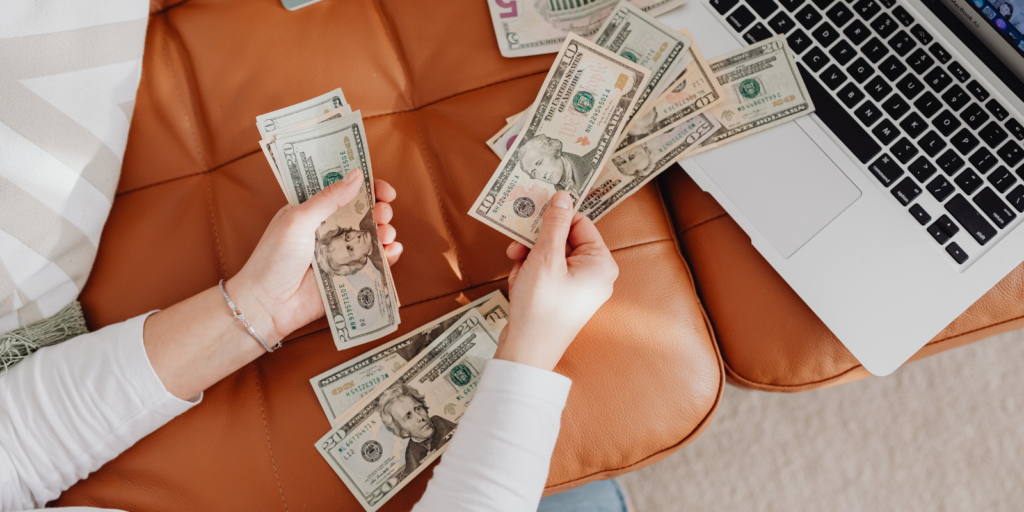 A Woman counting money in front of a laptop.