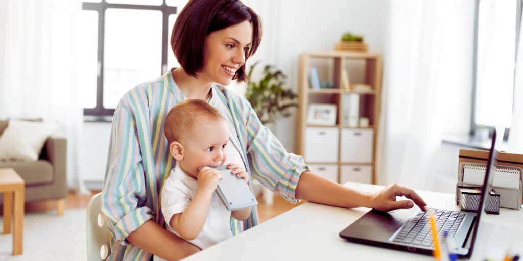 A working Mom working while holding a baby.